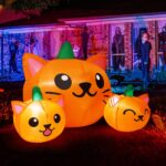 A 5-foot long Halloween inflatable featuring three orange and green pumpkin cat heads with bright white LED lights, set up ou