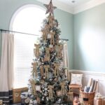 A close-up view of multiple light brown velvet ribbon bows, some hanging on a Christmas tree with soft, blurred lights in the