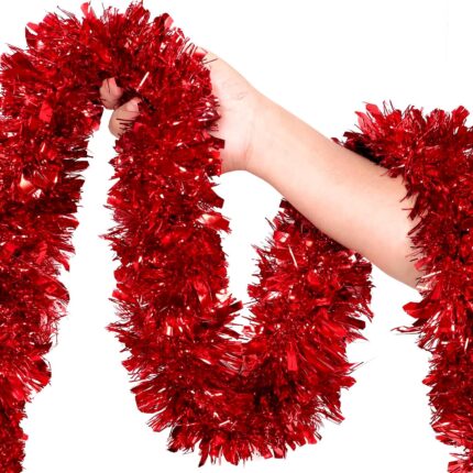 A long, vibrant red tinsel garland twisted and draped over a fireplace mantle with other Christmas decorations.
