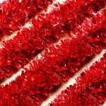 A long, vibrant red tinsel garland twisted and draped over a fireplace mantle with other Christmas decorations.