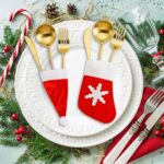 Close-up of red and white non-woven Christmas mini Santa hats and stocking silverware holders on a holiday table.